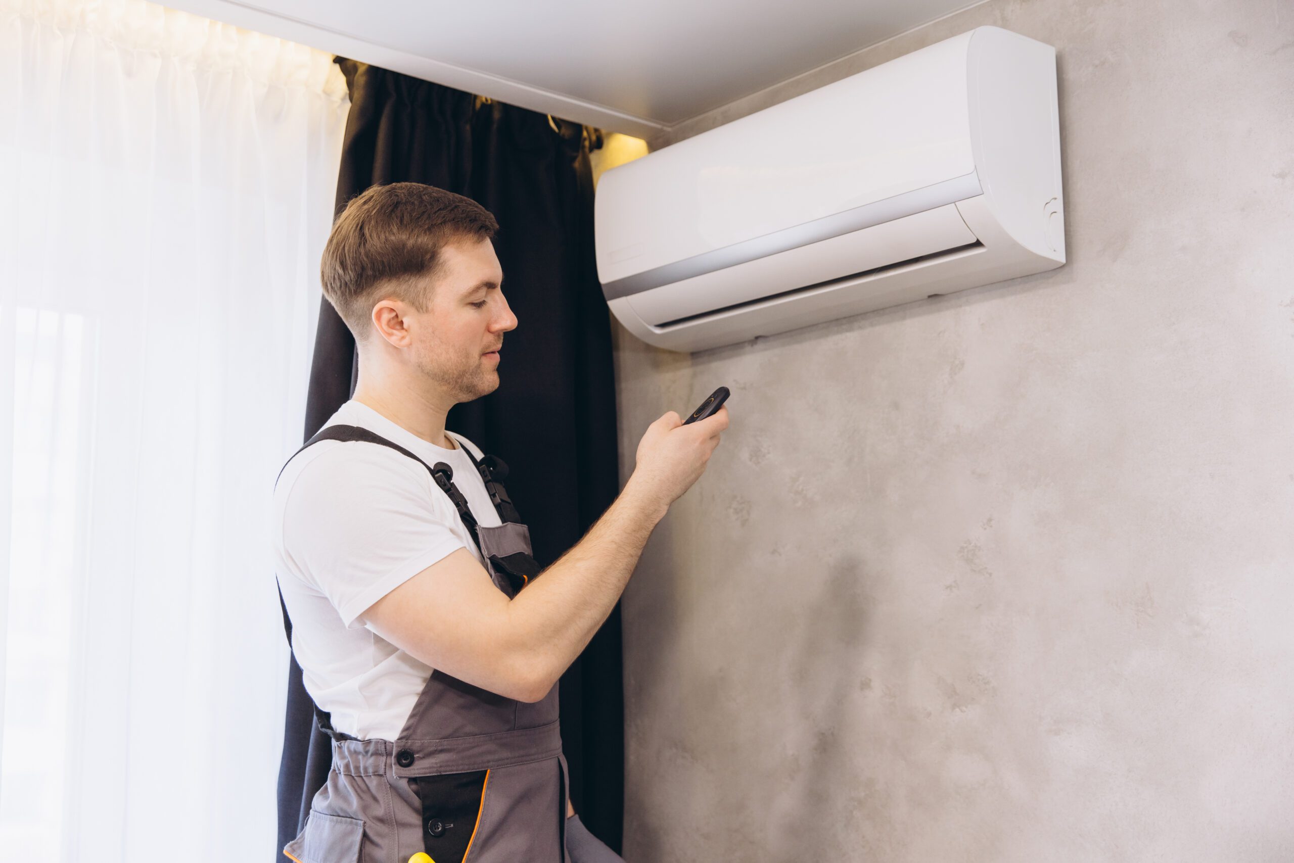 Technician using a remote control to control a wall mounted air conditioner Technician is using a remote control to operate a modern wall mounted air conditioning unit, ensuring optimal cooling performance
